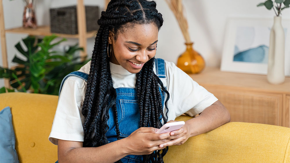 Pessoa sorridente interagindo com o celular em um ambiente acolhedor, mostrando como aprender outro idioma pode ser leve e parte da rotina diária com o uso de apps.